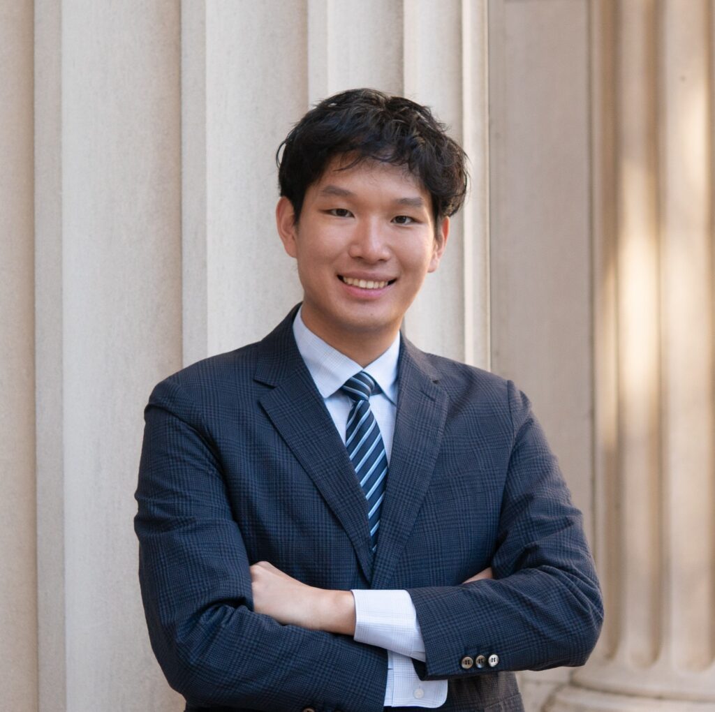 Zhiling Zheng stands in front of column wearing a dark suit.