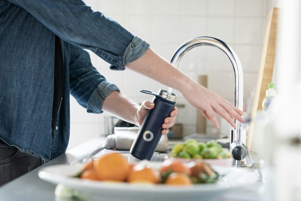 an individual fills up a water bottle at the kitchen faucet